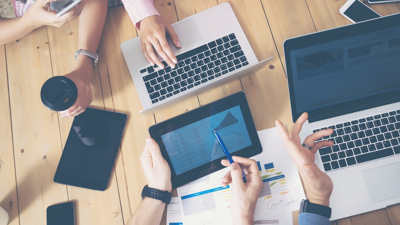 Generisches Büro, mehrere Hände die über einen Tisch greifen Laptops und Tablets auf dem tisch Kachel Vorschau
